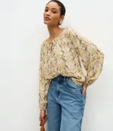 Blusa de manga larga con estampado geométrico en tonos verdes y violetas, cuello redondo con detalle de amarre frontal y puños elásticos.