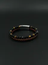 Pulsera doble para hombre que combina una tira de cuero trenzado marrón con una hilera de cuentas de piedra natural en tonos negros, marrones y grisáceos. Cuenta con un cierre magnético de acero inoxidable.