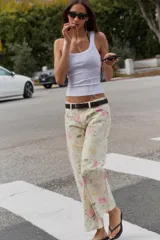 Jeans de tiro bajo y corte suelto con diseño de cinco bolsillos, trabillas para cinto y cierre frontal con cremallera y botón metálico, adornado con un estampado floral en tonos rosados y verdes sobre base clara.