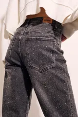 Jean de tiro alto, corte recto y largo al tobillo, en color negro lavado con apliques de strass o brillos distribuidos por toda la prenda.