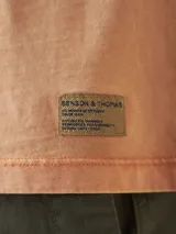 Camiseta de manga corta color naranja claro, con cuello redondo y un bolsillo en el pecho. Presenta un efecto de teñido en prenda que le da un aspecto ligeramente desgastado.