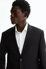 Blazer negro de corte entallado, confeccionado en tejido suave con solapas de muesca finas, un botón de cierre frontal, bolsillos con solapa y bolsillo superior en el pecho.