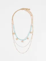Collar triple de estilo delicado, compuesto por tres cadenas de diferente diseño en tono dorado. Una de las cadenas presenta pequeñas cuentas celestes intercaladas con dijes de flores doradas, mientras que las otras dos son cadenas simples y finas.