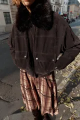 Chaqueta estilo bomber de corte oversize en color marrón oscuro, confeccionada con acabado aterciopelado. Presenta un cuello de solapa con detalle de pelo sintético desmontable, cierre frontal oculto con cremallera y botones a presión, bolsillos delanteros con solapa y bajo elástico.