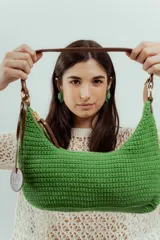 Cartera de hombro tejida a mano en crochet color verde, con asa y detalles en cuero marrón y cierre superior.