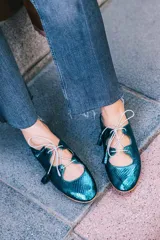 Zapato tipo blucher con diseño híbrido de bailarina, confeccionado en piel azul con textura de reptil. Presenta cierre con cordones y borlas de piel, con una banda elástica en la parte trasera para un ajuste óptimo. Cuenta con suela de cuero y acabado artesanal.