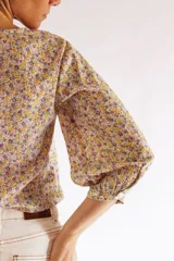 Blusa cruzada con estampado floral en tonos de lila, amarillo y verde. El cruce se ajusta a la cintura con un lazo. Tiene mangas 3/4 con puños elásticos y escote en V.
