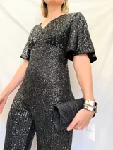 Mono corto de fiesta con lentejuelas negras, escote en V, mangas cortas acampanadas y espalda descubierta con lazo.