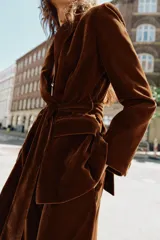 Blazer de terciopelo color marrón, con cuello solapa, manga larga y cierre frontal cruzado con botones. Incluye bolsillos con solapa en el delantero y un cinturón del mismo tejido para ajustar a la cintura.