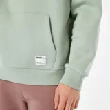 Buzo de felpa con capucha de color verde menta, corte holgado, bolsillo tipo canguro delantero con etiqueta pequeña cosida y cordones ajustables en la capucha.