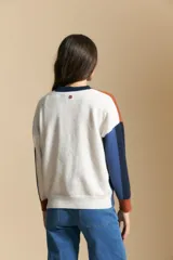 Sweater de tejido de punto con diseño geométrico de bloques de color en tonos tierra, marrón, ocre y blanco. Presenta cuello redondo, mangas largas y un corte relajado.