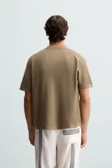 Camisa de punto color marrón, de corte relaxed fit, con cuello solapa, manga corta y acabados en rib. Cierre frontal de botonadura.