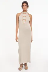 Vestido largo de tejido de punto color visón con escote halter y apliques circulares en relieve en el centro del pecho, de diseño recto y sin mangas.