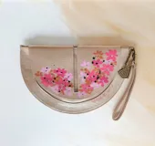 Sobre de mano en forma de media luna, confeccionado en cuero dorado brillante con textura efecto reptil y detalles de flores pintadas a mano. Cuenta con cierre superior y correa de muñeca incorporada.