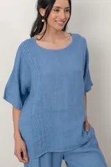 Blusa de lino color marrón oscuro, con escote redondo, mangas cortas amplias y detalle de alforzas verticales en el lateral derecho.