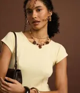 Vestido corto color amarillo pálido, con escote redondo y mangas cortas. Presenta recortes verticales en el torso que definen la silueta y una falda ligeramente acampanada.