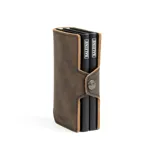 Billetera compacta de cuero sintético color marrón con doble compartimento de aluminio para tarjetas y bolsillo exterior con cierre metálico.