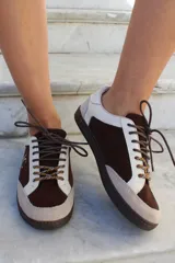 Championes de estilo urbano en combinación de tonos marrones y crema, confeccionados en gamuza y cuero. Presentan cordones jaspeados, suela de goma y detalle de logo bordado en el lateral.