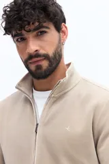 Campera de algodón color beige, estilo deportivo con cierre frontal, cuello alto y puños. Presenta bolsillos laterales y un pequeño logo bordado en el pecho.