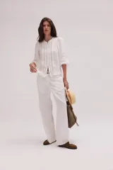 Pantalón de lino lavado color beige, de calce recto y diseño relajado. Presenta cintas de lino desflecadas aplicadas en los laterales con pespunte central, pretina con botón metálico, bolsillos delanteros y traseros.