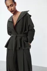 Trench corto de corte fluido confeccionado en mezcla de lyocell, color verde militar. Presenta cuello solapa, cierre frontal cruzado con botón, mangas largas con hombro caído y puños con trabilla. Incluye bolsillos delanteros de plastrón y cinturón de lazada en el mismo tejido.