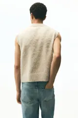 Chaleco de punto color beige claro con acabado afelpado o peludito, cuello en V y corte holgado.