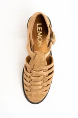 Sandalias cangrejeras de gamuza color visón, con diseño de tiras entrelazadas, tira ajustable con hebilla metálica en el tobillo y suela plana de goma marrón.