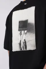 Remera de corte oversize confeccionada en algodón premium color crudo. Presenta un bordado frontal con la inscripción '90's' en color negro y un parche gráfico en la espalda con estética retro inspirada en los años 90.