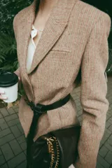 Blazer de corte clásico con cuello solapa y manga larga, confeccionado en tejido con patrón de espiga en tonos tierra y líneas verticales en color salmón. Cuenta con bolsillos delanteros y cierre frontal con botones ocultos.