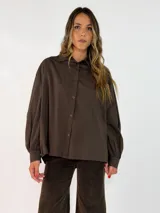 Camisa de corte oversize color marrón chocolate, con cuello clásico, cierre frontal de botones y mangas largas abullonadas con puños ajustados.
