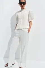 Blusa de cuello redondo con detalle de volados, manga corta abullonada con terminación elástica y cierre frontal con botones. Presenta un diseño de tejido plisado en toda la prenda.