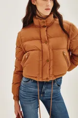 Campera puffer color tostado, con cierre frontal y botones a presión, cuello alto y puños tejidos acanalados.