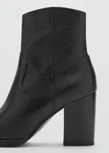 Botín de cuero vacuno color negro, con diseño de estilo western, punta fina y tacón bloque de 6,5 cm. Cuenta con cierre de cremallera lateral.