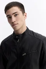 Campera de cuero sintético color negro, con cuello mao, cierre frontal y bolsillos laterales con cierre. Presenta detalles de costuras acolchadas en los hombros y un bolsillo pequeño con cierre en el pecho.