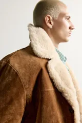 Campera marrón de piel con interior de borreguillo color crudo, de corte regular fit, con cuello bowling, bolsillos de doble vivo y cierre frontal con botones.