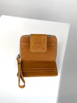 Mini billetera de cuero marrón con solapa frontal que presenta un grabado de un búho. El cuerpo de la billetera está confeccionado en cuero con pelo natural en tonos marrones y manchas doradas.