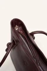 Bolso tipo tote color marrón de cuero suave, con doble asa larga decorada con nudos en los extremos inferiores y detalle de logo grabado en el frente.