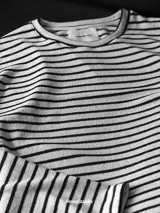 Buzo de tela fina, liviano y cómodo, con estampado de rayas horizontales blancas y negras, cuello redondo y puños acanalados.