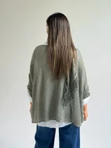 Sweater de punto color verde oliva con diseño de paneles horizontales de encaje floral, corte holgado y mangas tres cuartos. Incluye una bufanda del mismo tono y tejido, y se presenta superpuesto sobre una camisa blanca de cuello clásico.