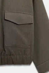 Cazadora de cuello solapa y manga larga, color verde militar, con bolsillos delanteros de plastrón con solapa, bajo elástico y cierre frontal con cremallera.