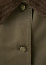 Chaqueta verde militar corta con cuello camisero de pana marrón oscuro, cierre frontal de botones, bolsillos aplicados en el pecho y diseño holgado.