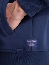 Canguro con cierre frontal completo, confeccionado en tejido fleece de color azul marino. Presenta capucha con cordones ajustables, bolsillos laterales y puños y ruedo acanalados.
