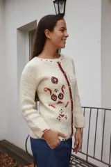 Saco de lana merino color blanco crudo, tejido a mano con dos agujas y detalles bordados artesanales en tonos rojo, negro y beige. Cuenta con cuello redondo y cierre frontal de botones de madera.