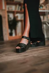 Sandalias altas negras de rafia con plataforma y taco chino. Tiras cruzadas al frente y hebilla de cuero en el contorno del tobillo.