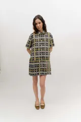 Vestido camisero corto con estampado a cuadros en tonos verde, azul y rojo. Presenta cuello camisero, mangas corta, cierre frontal con botones y falda tableada de corte bajo.