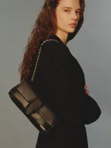 Cartera de cuero de cordero color blanco de silueta rectangular, con solapa frontal, cierre magnético y correa de cadena combinada con cuero trenzado. Incluye el logotipo de la marca grabado en dorado en el frente.