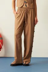 Pantalón marrón de corte recto, con cintura elastizada y cordón ajustable. Presenta mostacillas decorativas en los laterales.