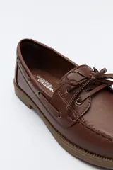Zapato náutico de cuero sintético color marrón, con cordones decorativos, costuras a la vista y suela de goma antideslizante.