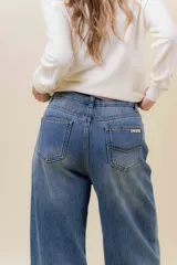 Jean de corte wide leg y tiro alto, confeccionado en denim rígido con un ligero efecto de desgaste. Presenta un diseño de calce relajado con pernera amplia, cintura marcada, bolsillos clásicos y cierre frontal con botón metálico.