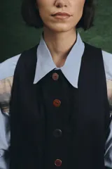 Mono largo de color negro con cierre frontal de botones vintage de distintos colores. Presenta un diseño sin mangas, con bolsillos laterales y una cinta para herramientas en la parte trasera.